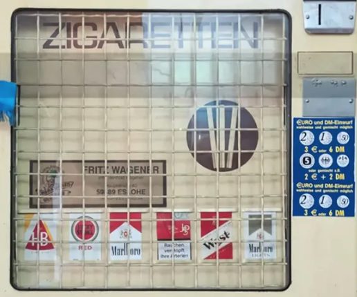 Alter cremefarbener Zigarettenautomat mit Gittertür, Schriftzug „Zigaretten“ und Münzeinwurf für Euro und DM